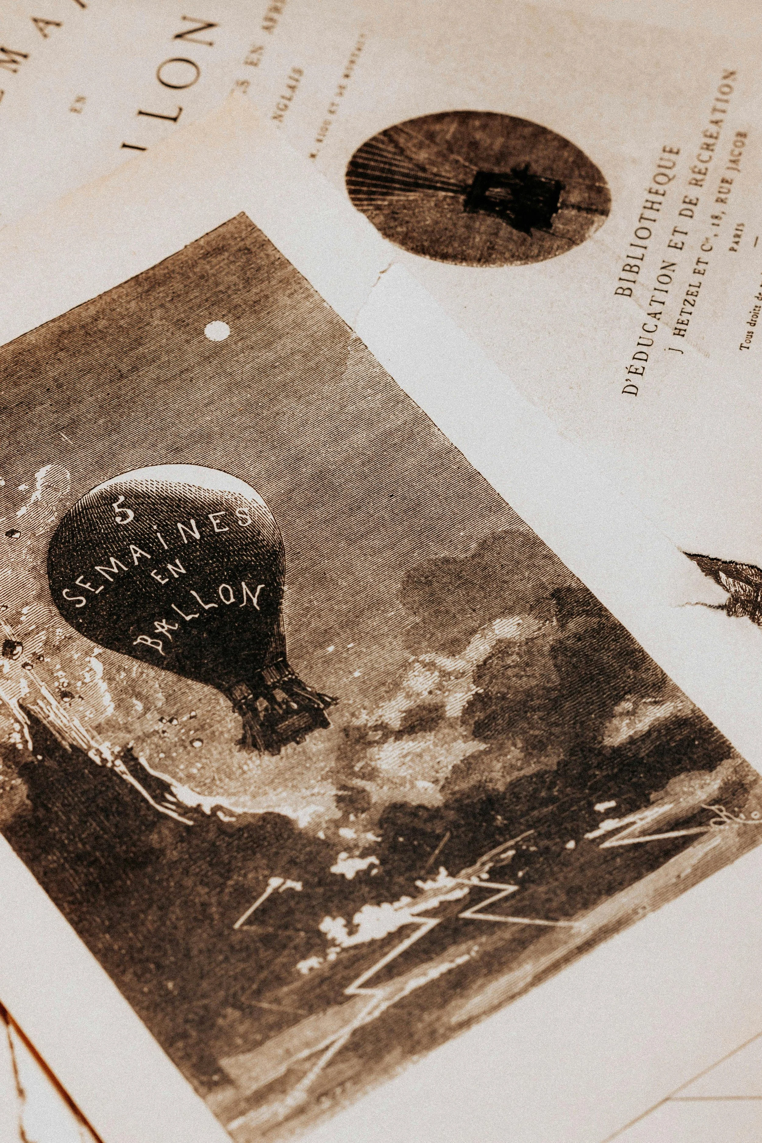 Black and white photograph of a hot air balloon in the sky with the text "5 SEMAINES EN BALLO" on it, with clouds and landscape below.