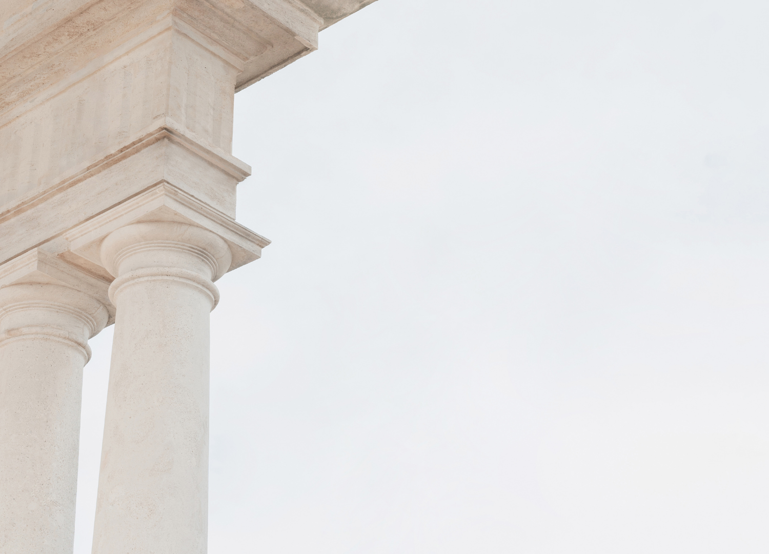 Close-up of two classical stone columns supporting a building with a cloudy sky in the background.
