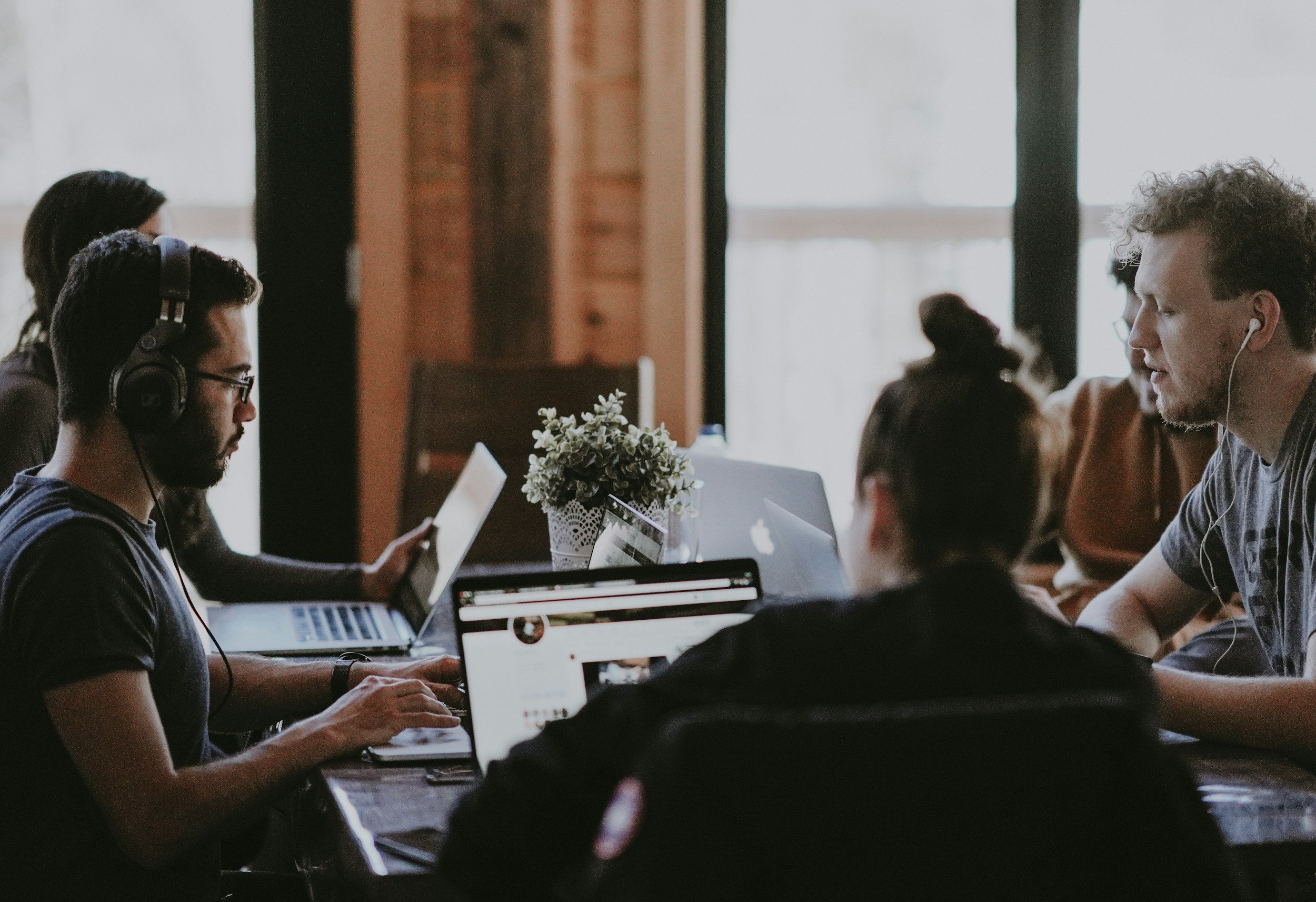 Group of people working at a table with laptops and tablets in a modern office.