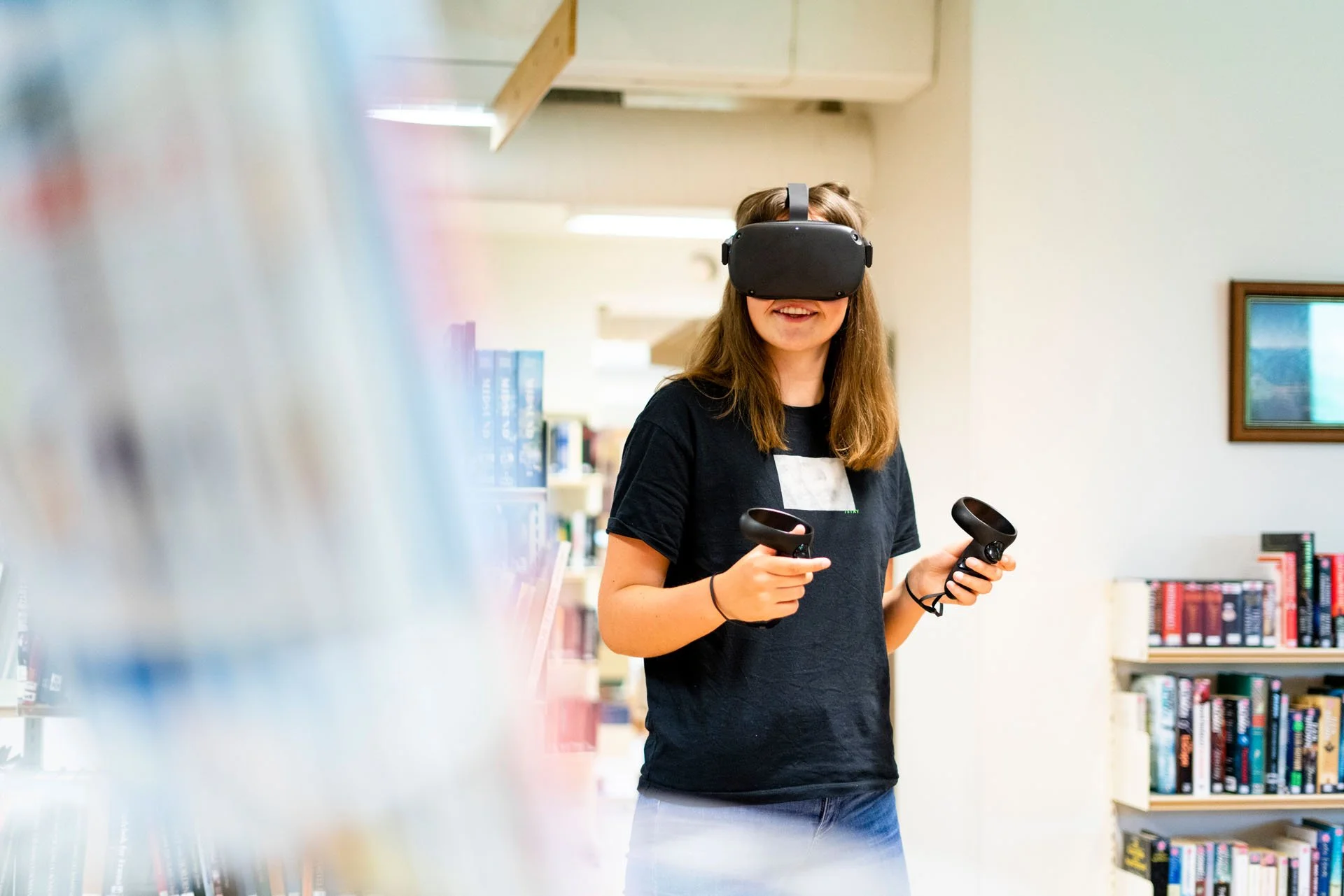 En ung jente i en bibliotek, iført en VR-hjelm og holder to VR-kontroller.