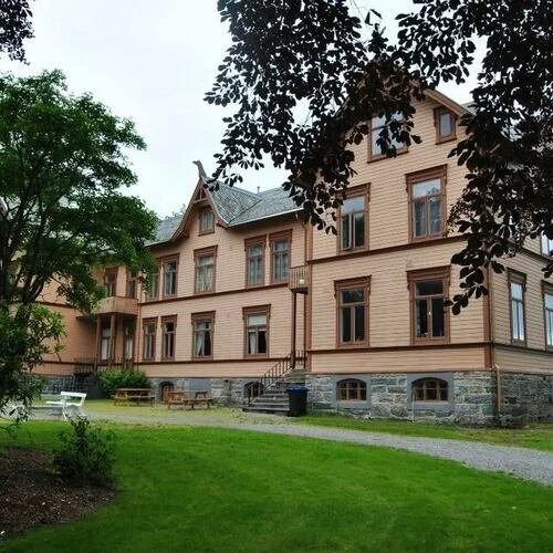 Utendørs bilete fra Gjermundnes museum. Ein eldre trebygning i sveitserstil, med beige veggar, brune vinduskarmar og steinmur