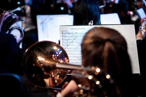 Bilde tatt bakfra av musikere med blåseinstrumenter/messingblåsere, med notestativer.