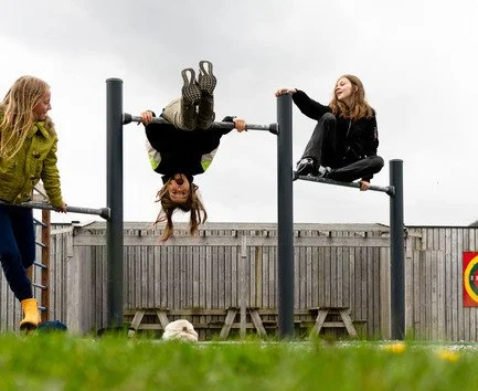 Tre barn som leker på en utendørs lekeplass, og turner å klatreapparater.