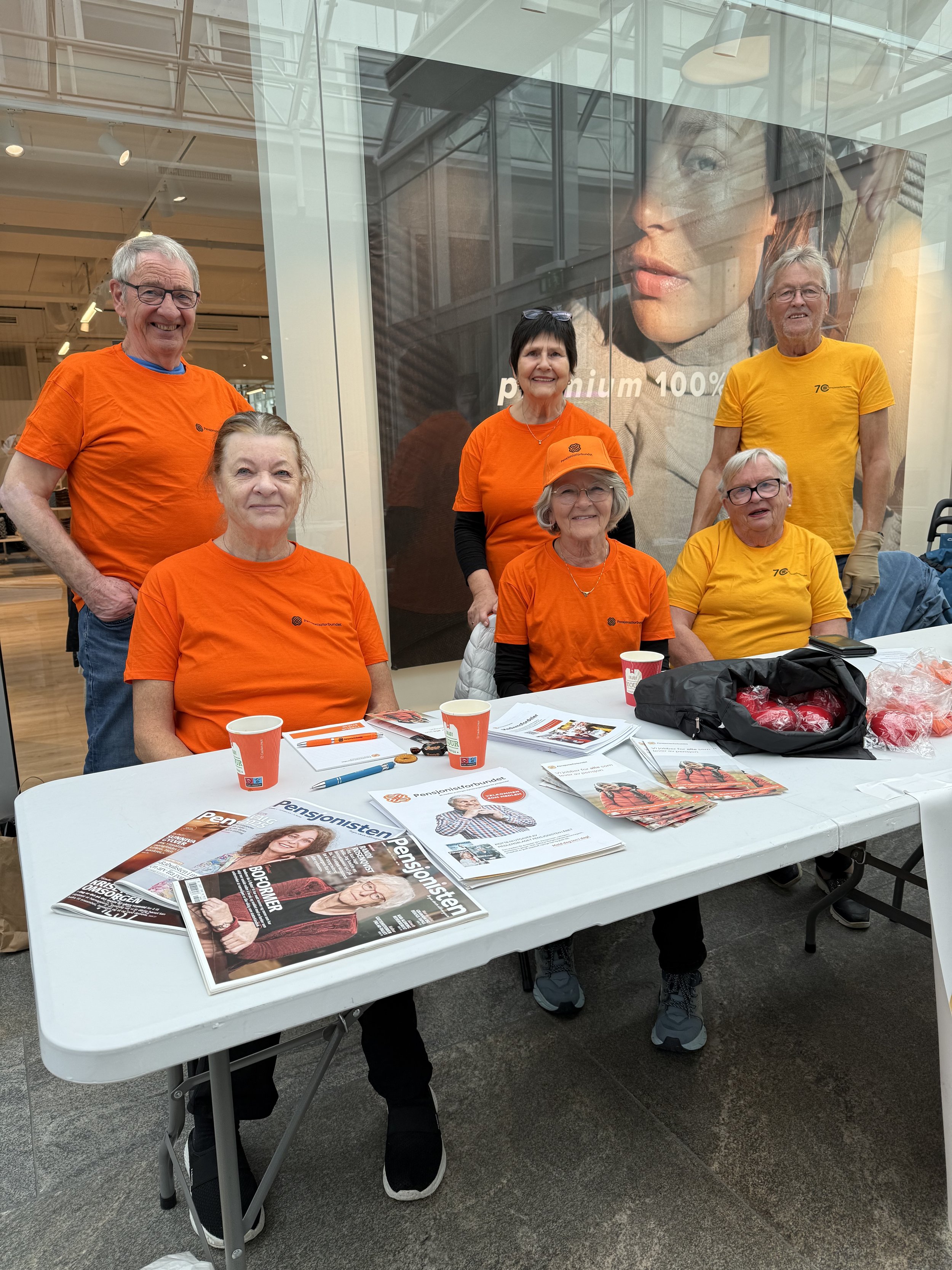 Ei gruppe eldre menneske sit rundt eit bord med eit banner hvor det står Pensjonistforbundet