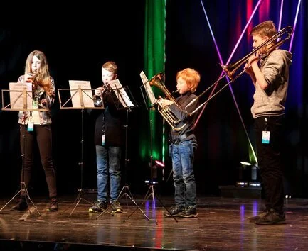 Fire barn og en voksen spiller på musikkinstrumenter på en scene med lyseffekt.