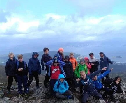 En gruppe ungdommer på fjelltur med utsikt over sjø og skyet himmel