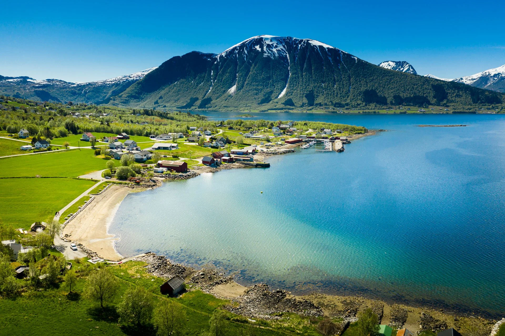 Fjell, hav, små bygninger, grønn natur, kystlinje, klar blå himmel.