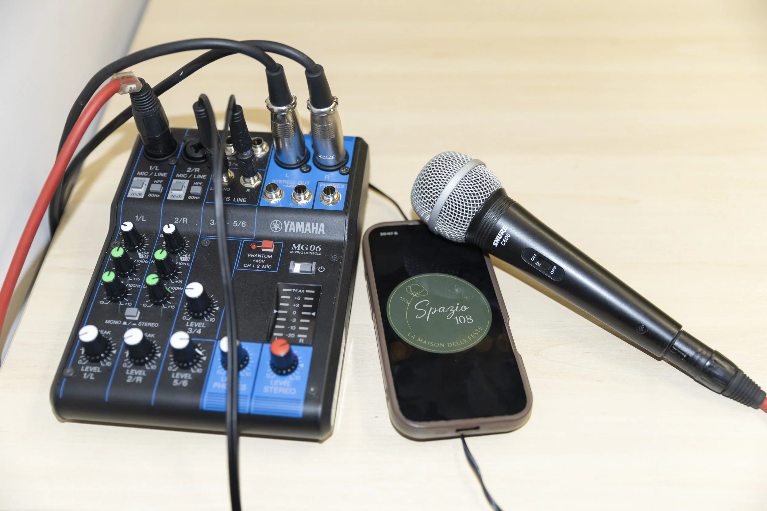 Mixer audio Yamaha MG06, microfono Shure, e smartphone su tavolo di legno