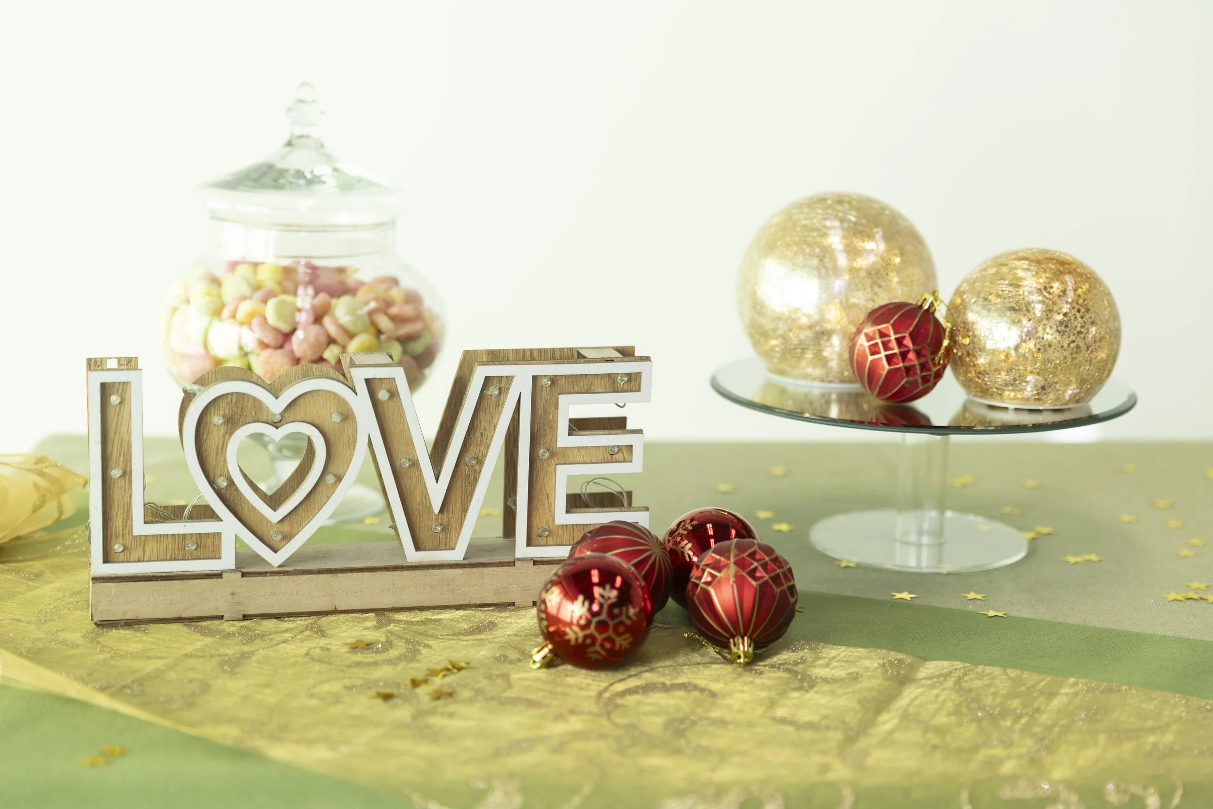 Decorazioni natalizie con oggetti rossi e oro, scritta LOVE in legno, ciotola con confetti colorati, stelle di carta dorate.