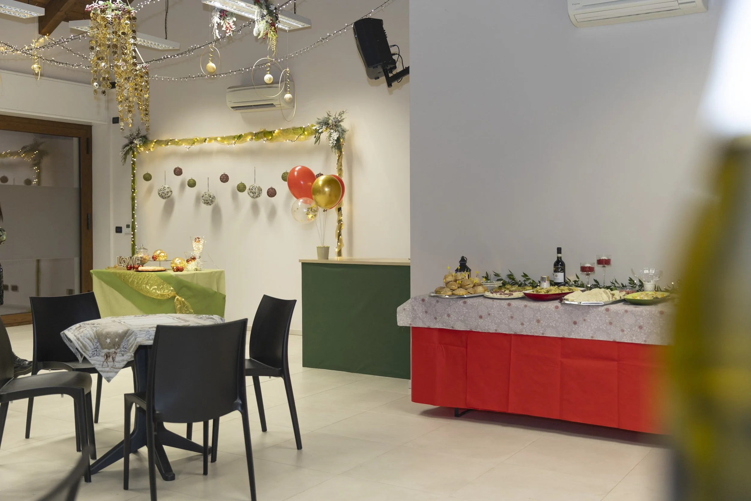 Decorazioni natalizie con palloncini, luci e addobbi, tavolo con cibo e bevande per festa, area con tavolo decorato con stoffa rossa e bianca