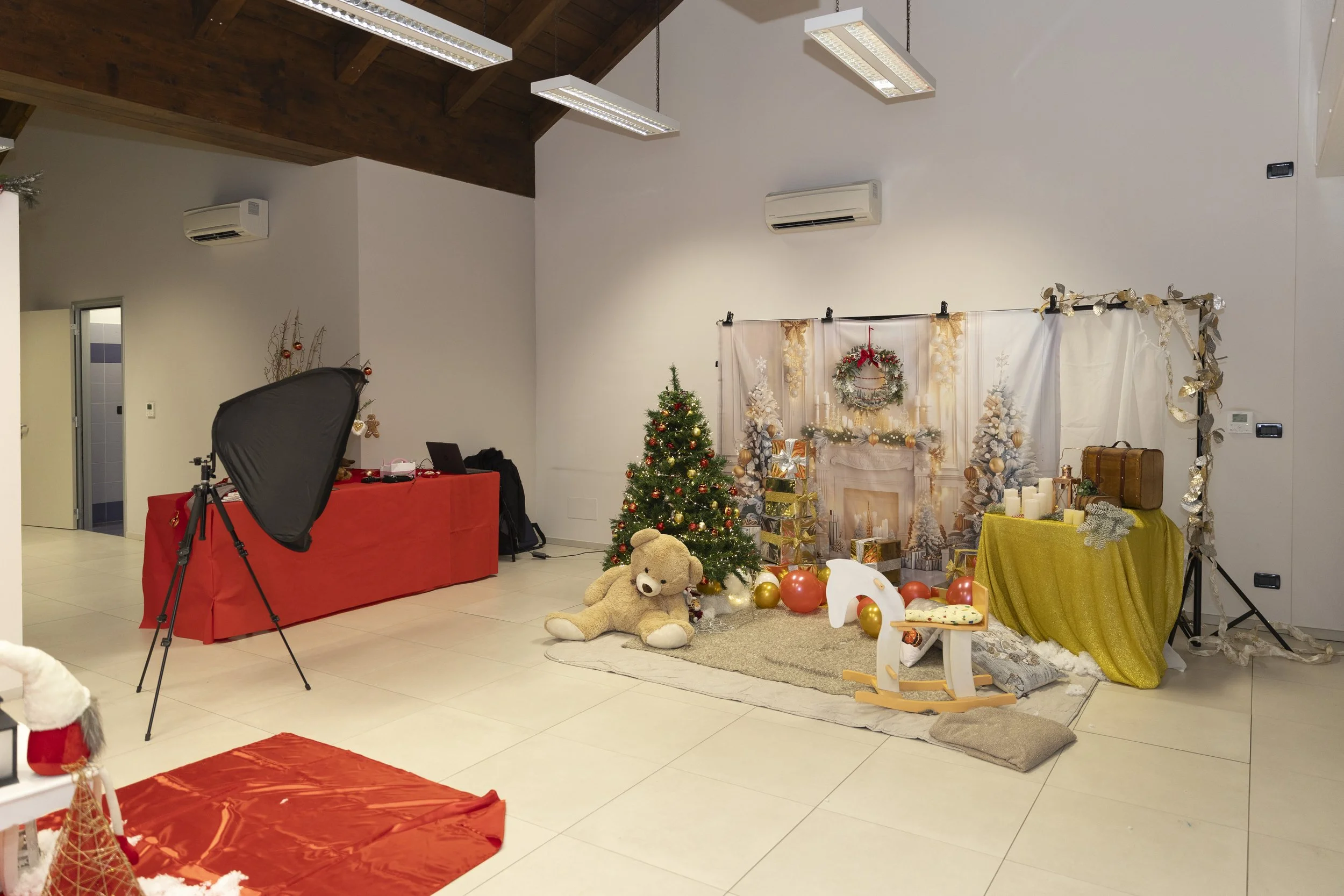 Setup natalizio con albero decorato, pupazzo di pezza, regali, decorazioni e sfondo di camino festivo, in uno spazio interno, probabilmente per fotografie di Natale.