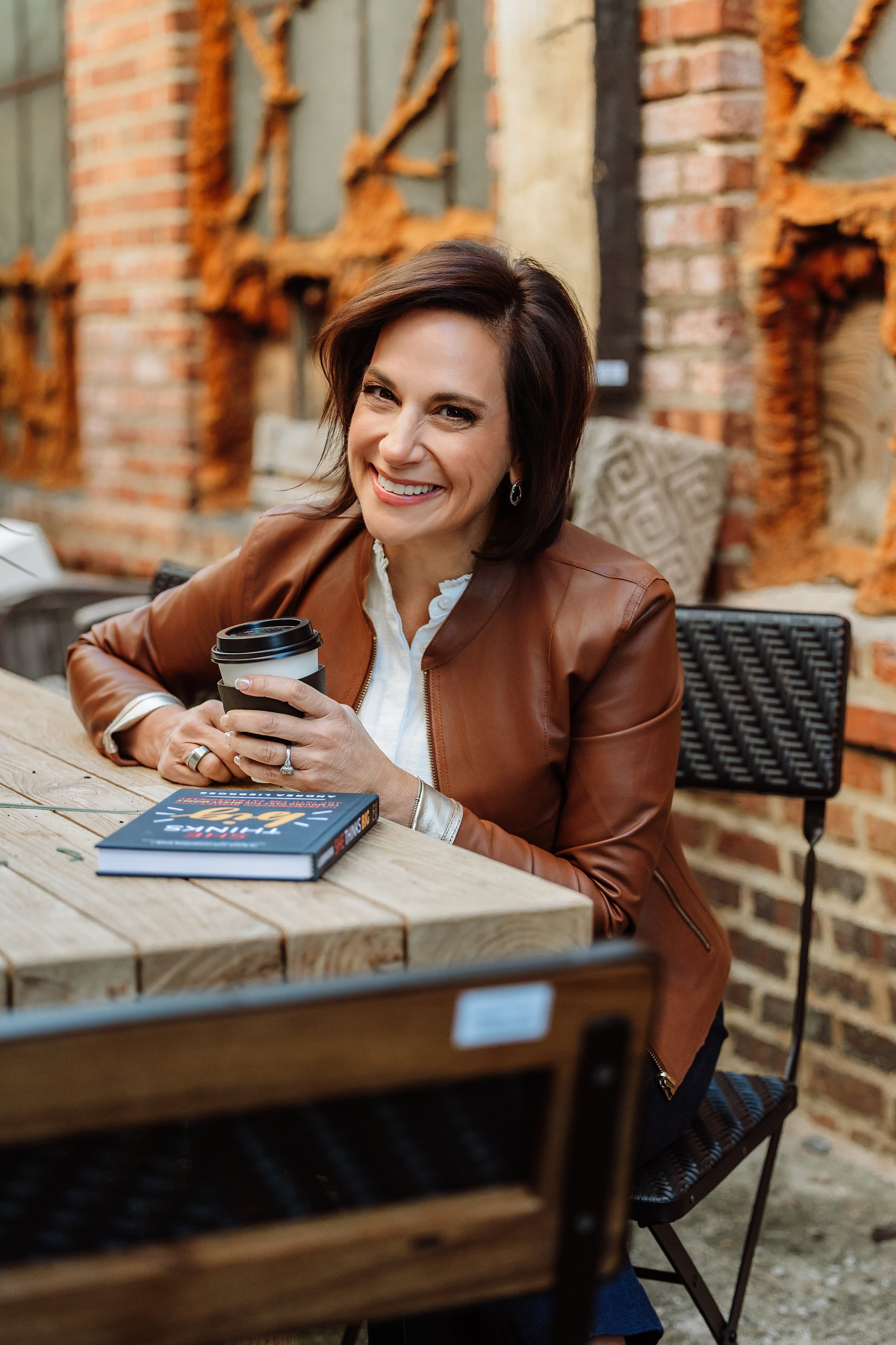 Andrea Liebross at coffee shop with She Thinks Big book