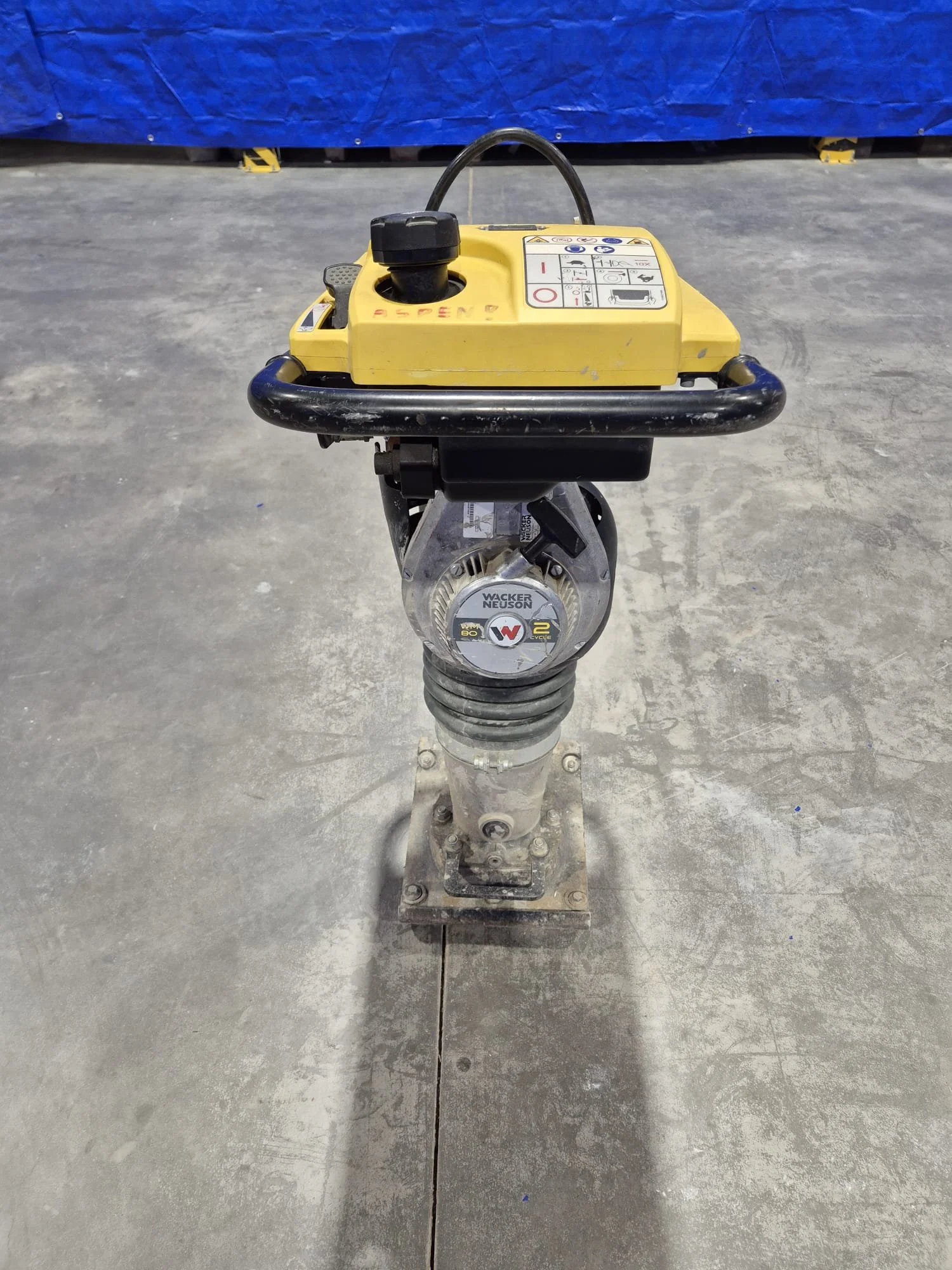 Ein gelber Vibrationsstampfer, der auf einem Betonboden befestigt ist, mit Anleitungen auf der Oberseite.