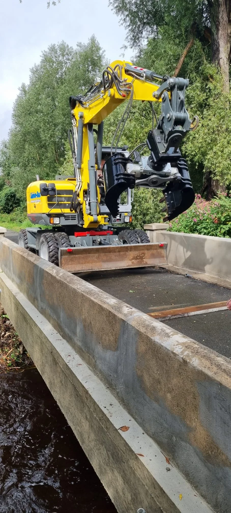 Ein Mobilbagger mit Greifarmeinrichtung, der auf einer Brücke über einem Fluss steht, zum Reinigen oder Reparieren der Brücke.