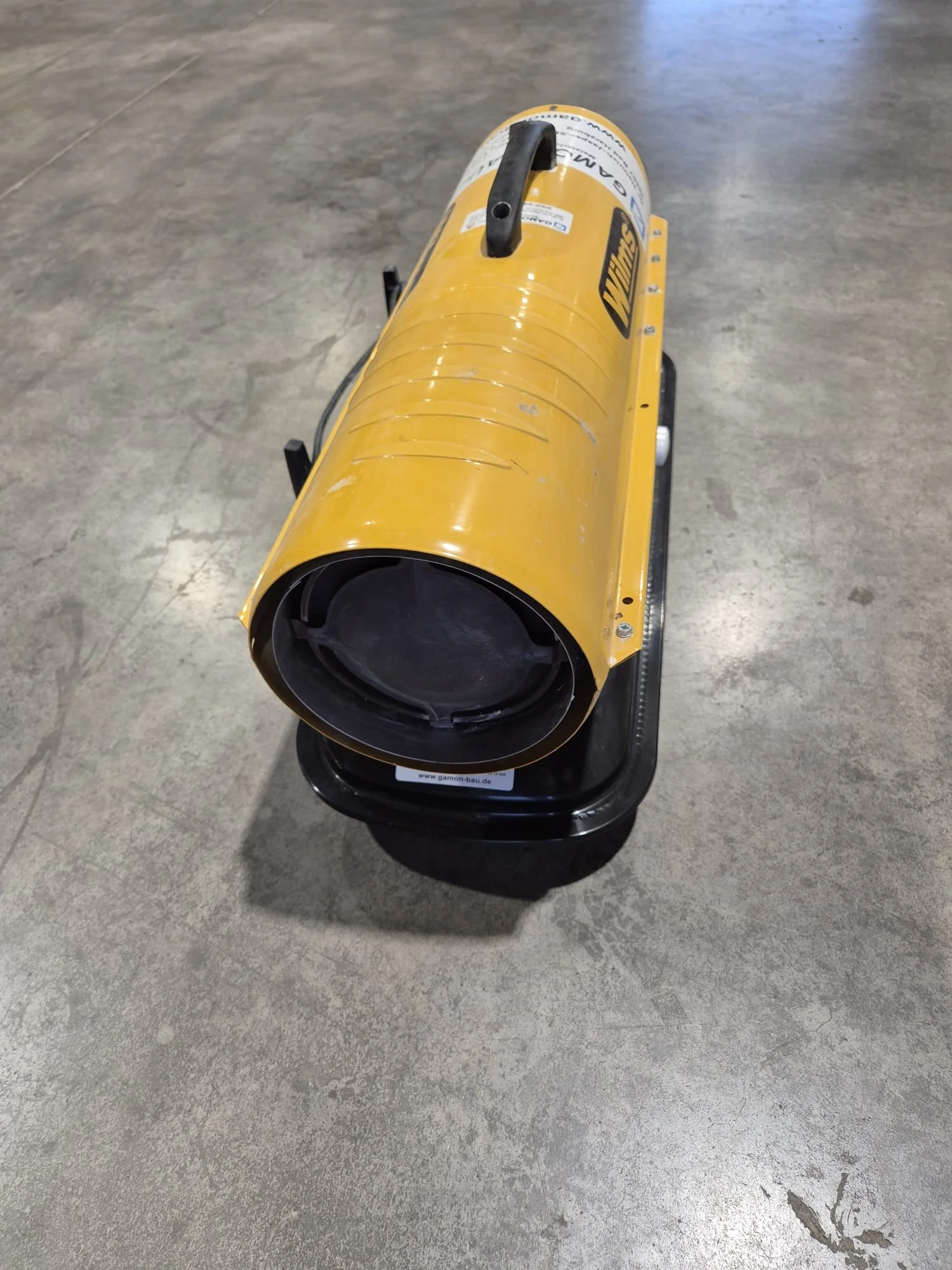 Bau-Lüfter auf einem Betonboden, gelber Farbton, runde Form, auf Tragegestell.