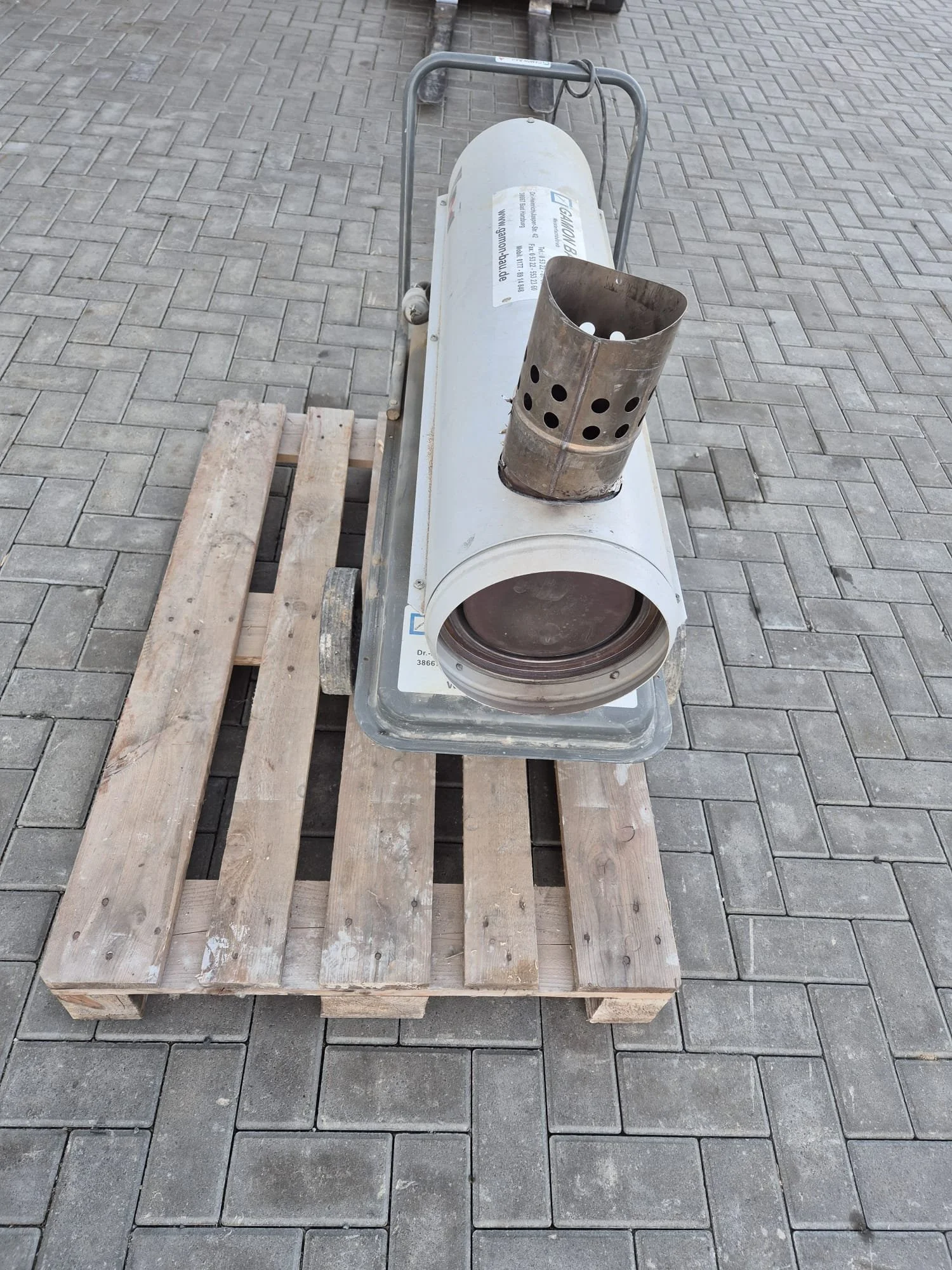 Ein Propangasofen auf einer Holzpalette, steht auf einem gepflasterten Boden.