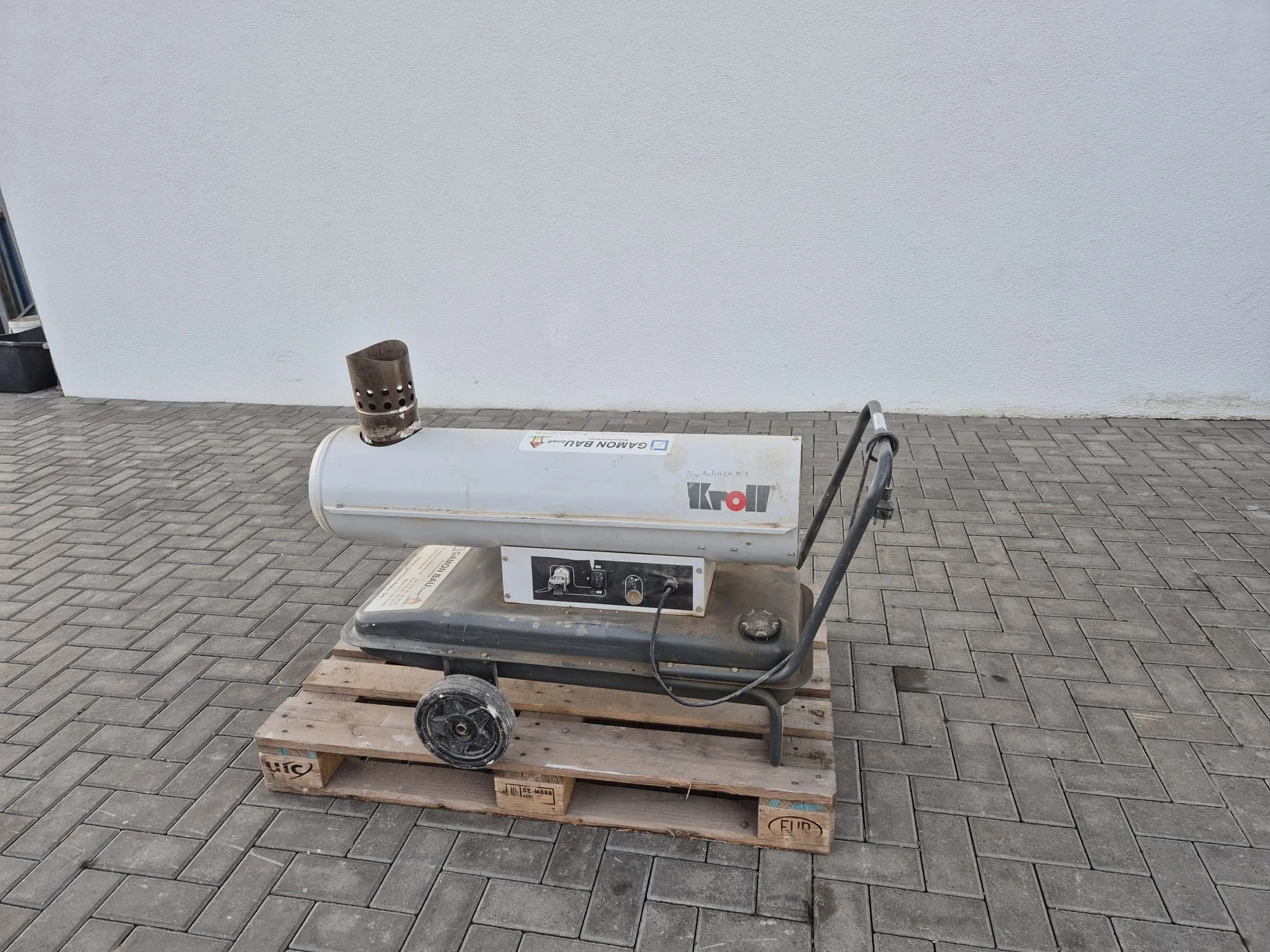 Ein Heizstrahler auf einer Palette vor einer weißen Wand.