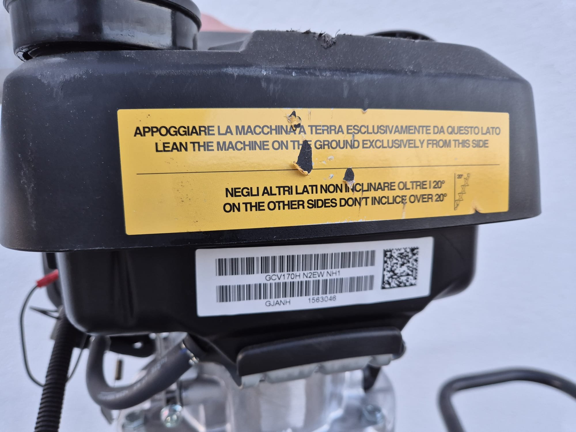 Ein Motorgerät mit einem gelben Warnhinweis in Deutsch und Englisch, das besagt, dass die Maschine nur auf der erdseitigen Seite geneigt werden darf, nicht über 20° auf den anderen Seiten.