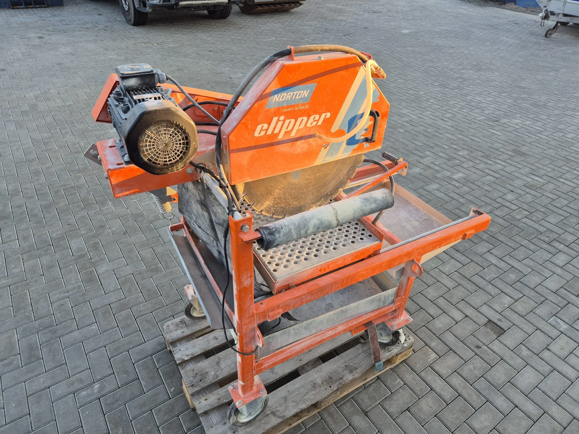 Eine orange Farbbeschichtete Kreissäge auf einem fahrbaren Wagen, die auf Kopf steht, mit einer städtischen Pflastersteinboden im Hintergrund.