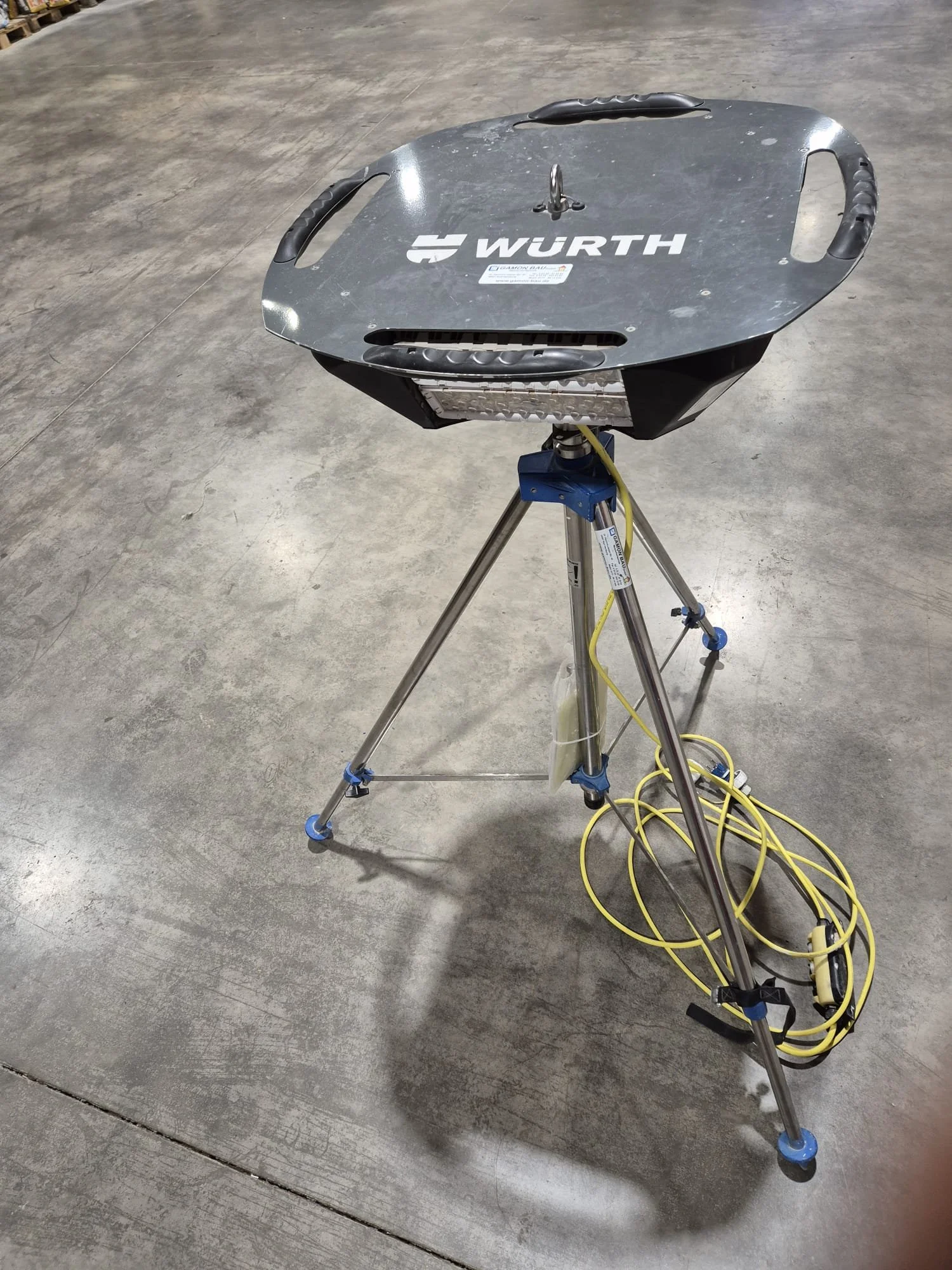 Ein Roboter mit einer schwarzen Metallplatte auf einem Dreibein-Stativ auf einem Betonboden.