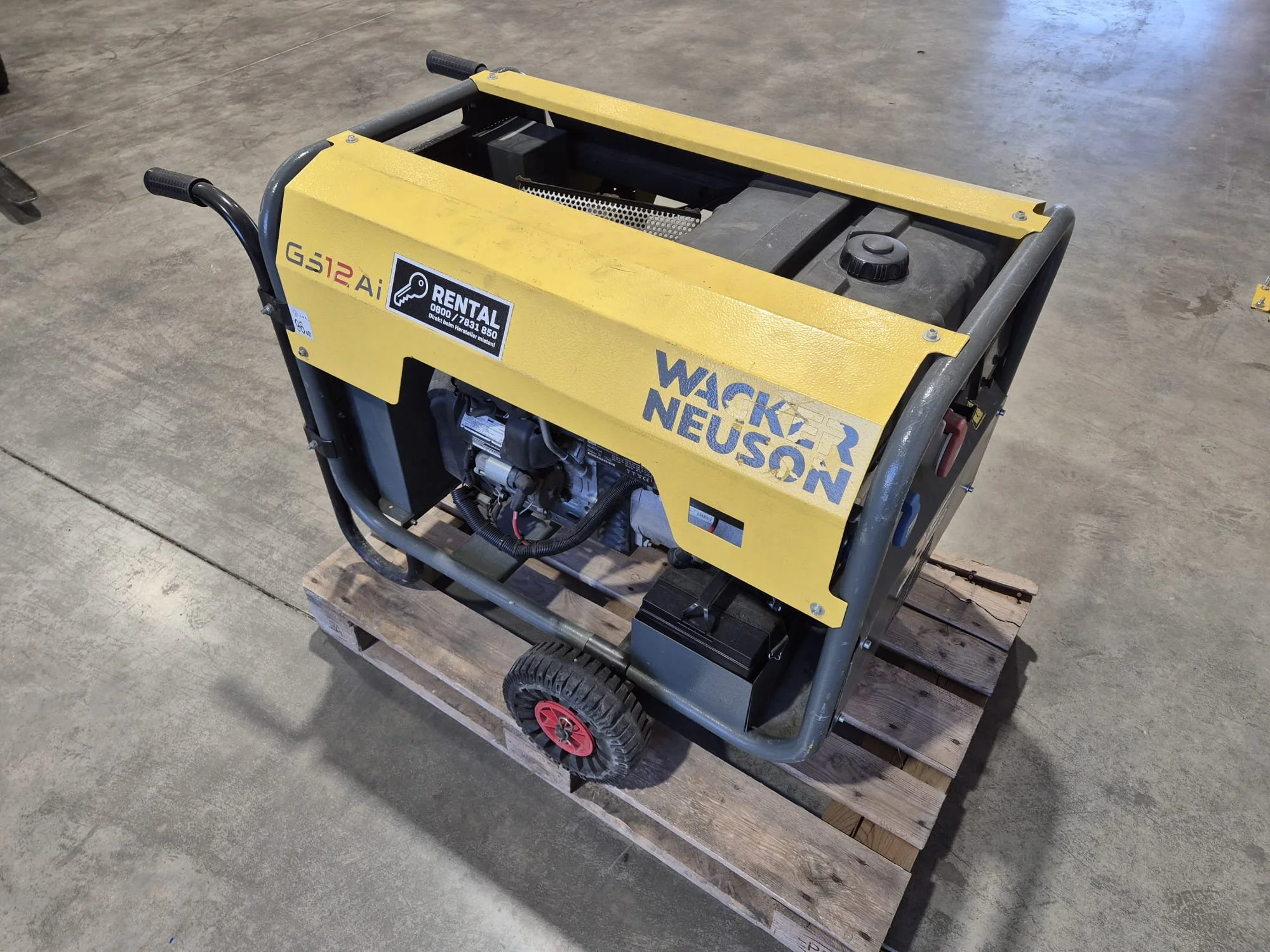 Ein gelber Baugenerator auf einer Holzpalette auf einem Betonschleiferboden.