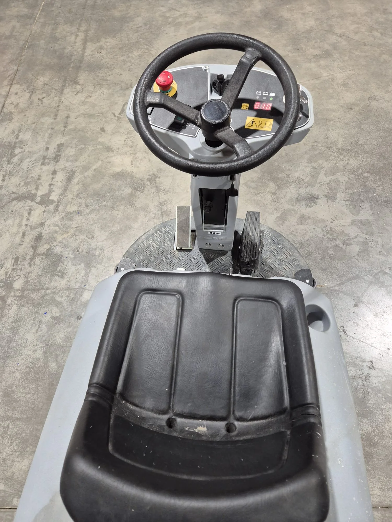 Vorneansicht eines elektrischen Gabelstaplers mit Lenkrad, Fußpedalen und Kontrollanzeigen, auf einem Betondeck