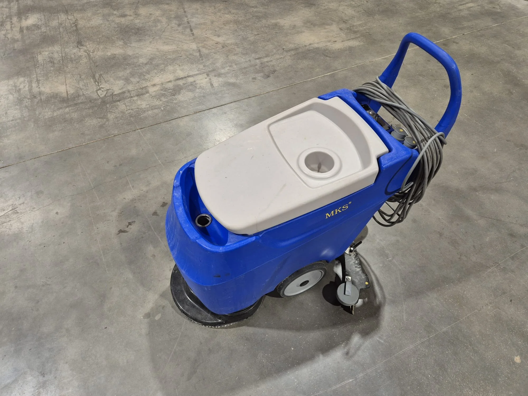 Ein blauer Bodenwischer mit grauem Wasserbehälter und elektrischem Kabel auf einem Betonboden.