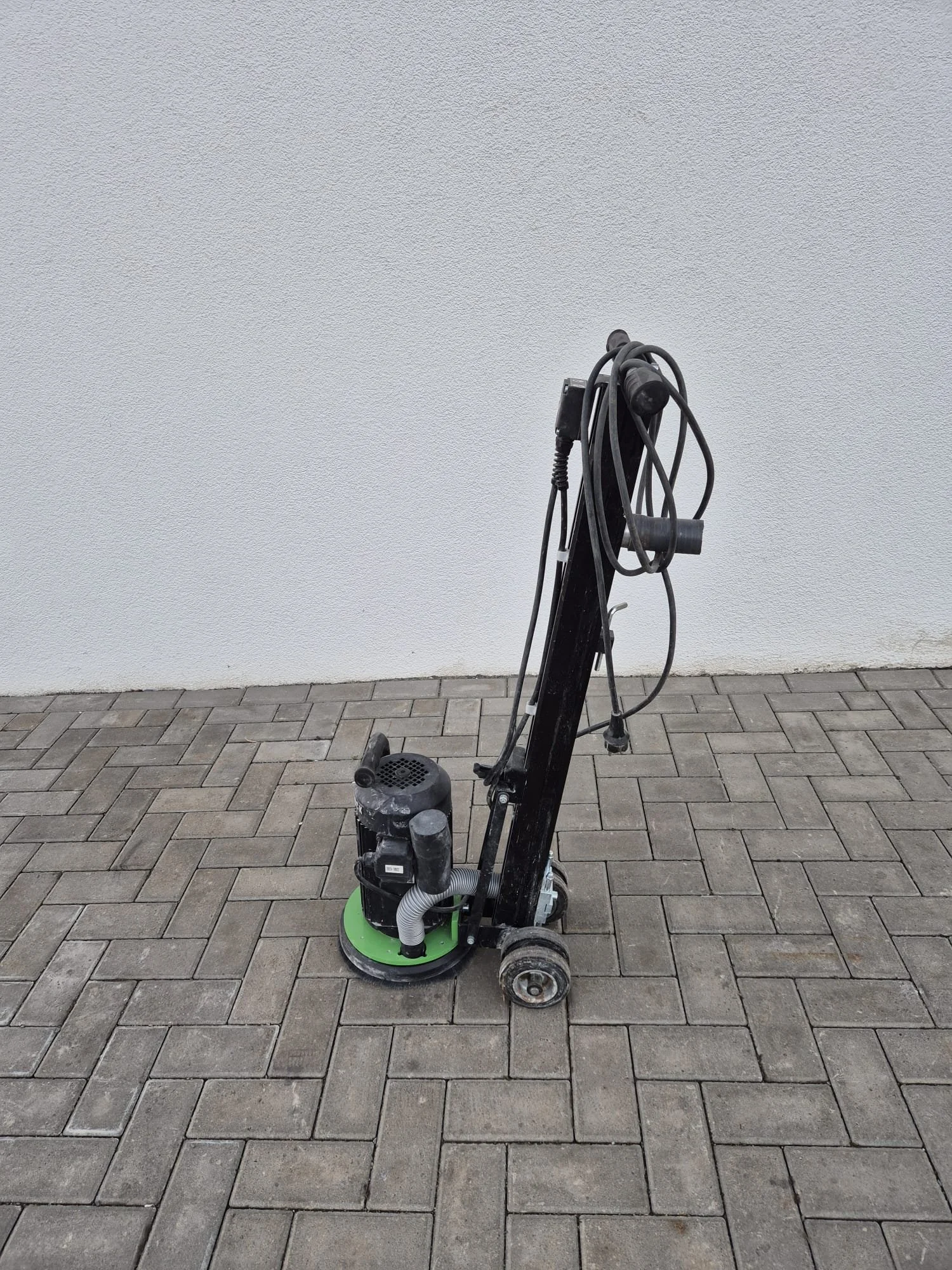 Ein Stromschleifgerät auf einer gepflasterten Oberfläche vor einer weißen Wand.