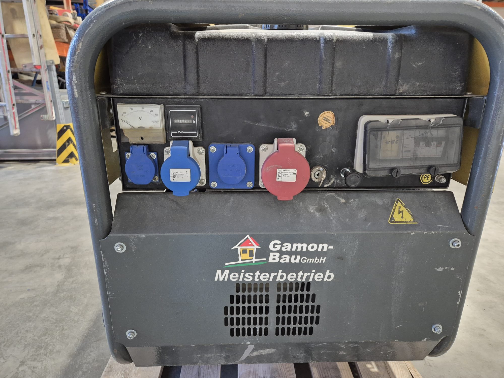 Batteriegenerator mit mehreren Steckdosen, einem Messinstrument, einem Kabelkasten, Kennzeichnungen und der Aufschrift "Gamon-Bau GmbH Meisterbetrieb".
