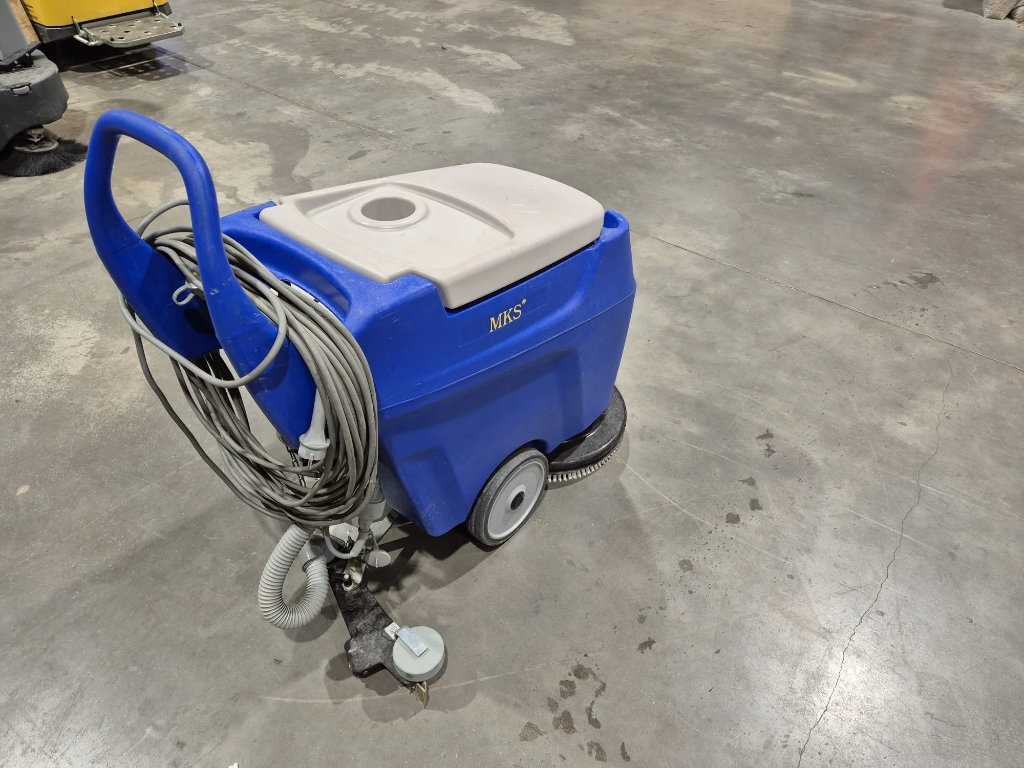 Ein blauer Reinigungswagen mit einem weißen Deckel steht auf einer Betonbodenfläche.