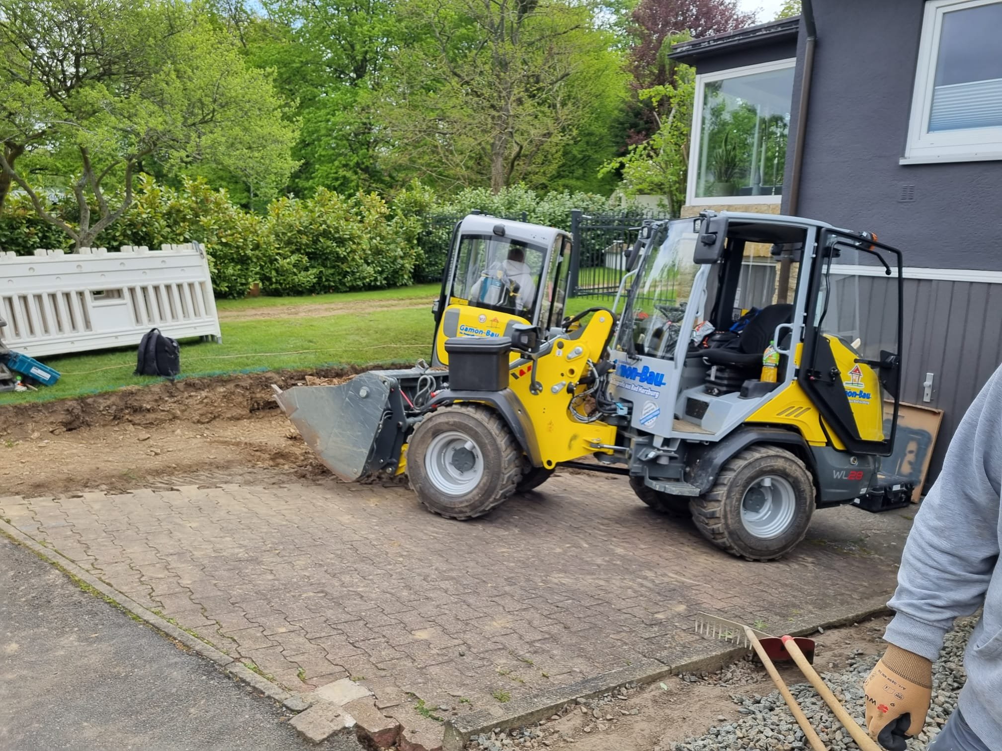 Bauarbeiter hebt in einem Garten mit einer Baumaschine den Boden aus, um eine Terrasse oder Einfahrt zu verbessern.