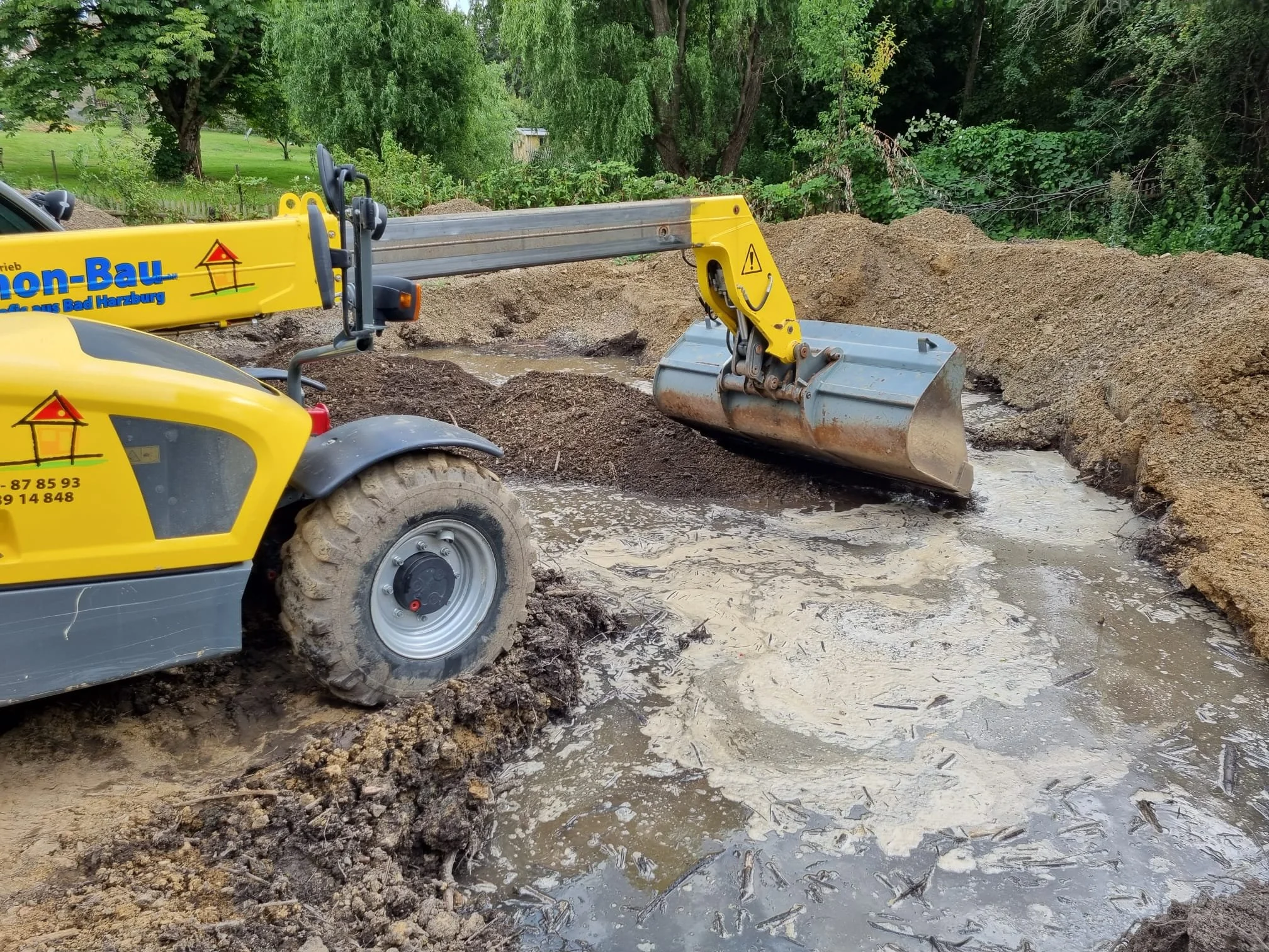 Baugerät Teleskoplader im Einsatz beim Aushub an einem Flussufer, um das Wasser abzuleiten.