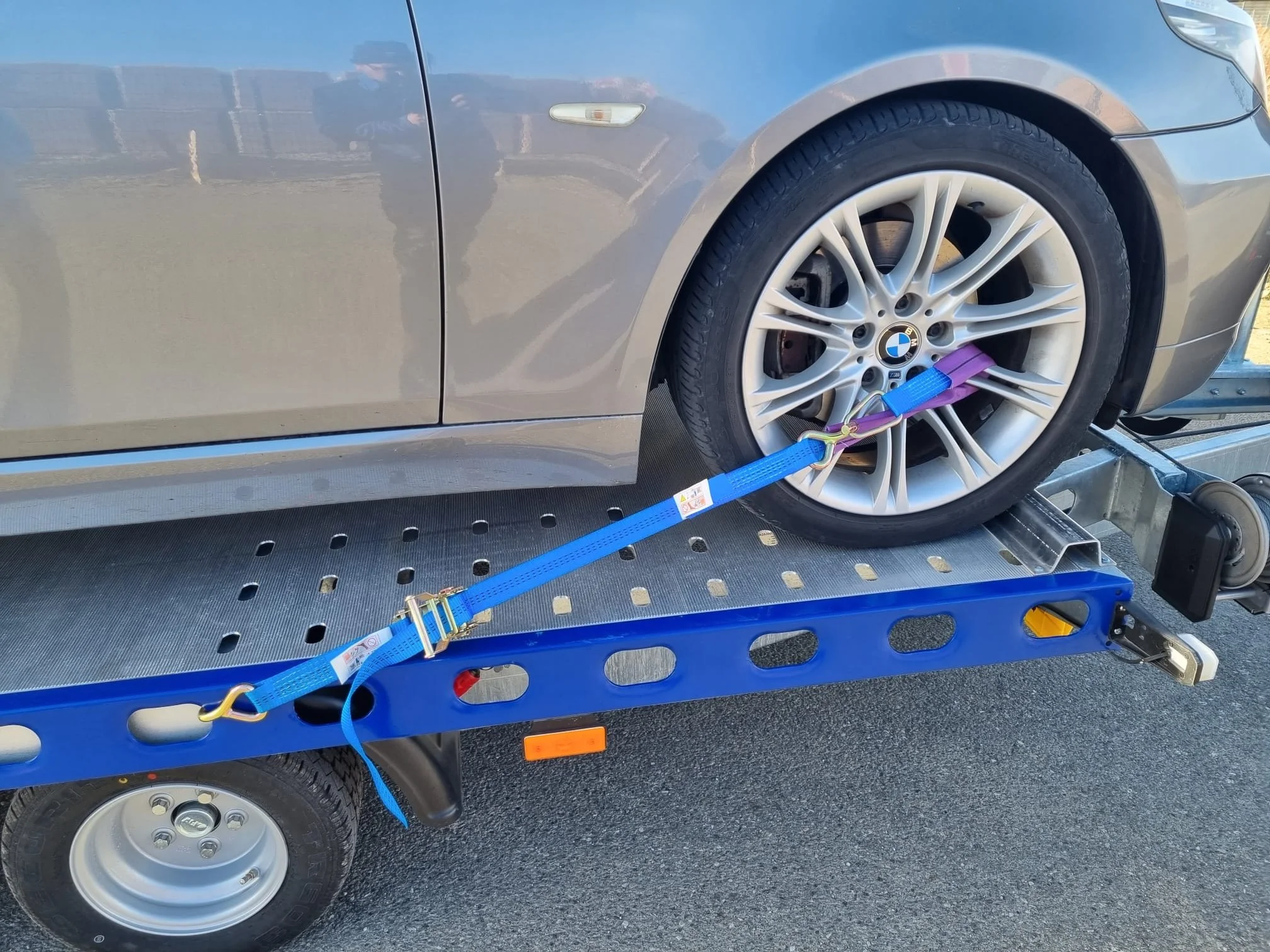 Ein BMW-Fahrzeug wird auf einem Abschleppwagen / Autotrailer transportiert. Das Auto ist mit Spanngurten am Rad gesichert.