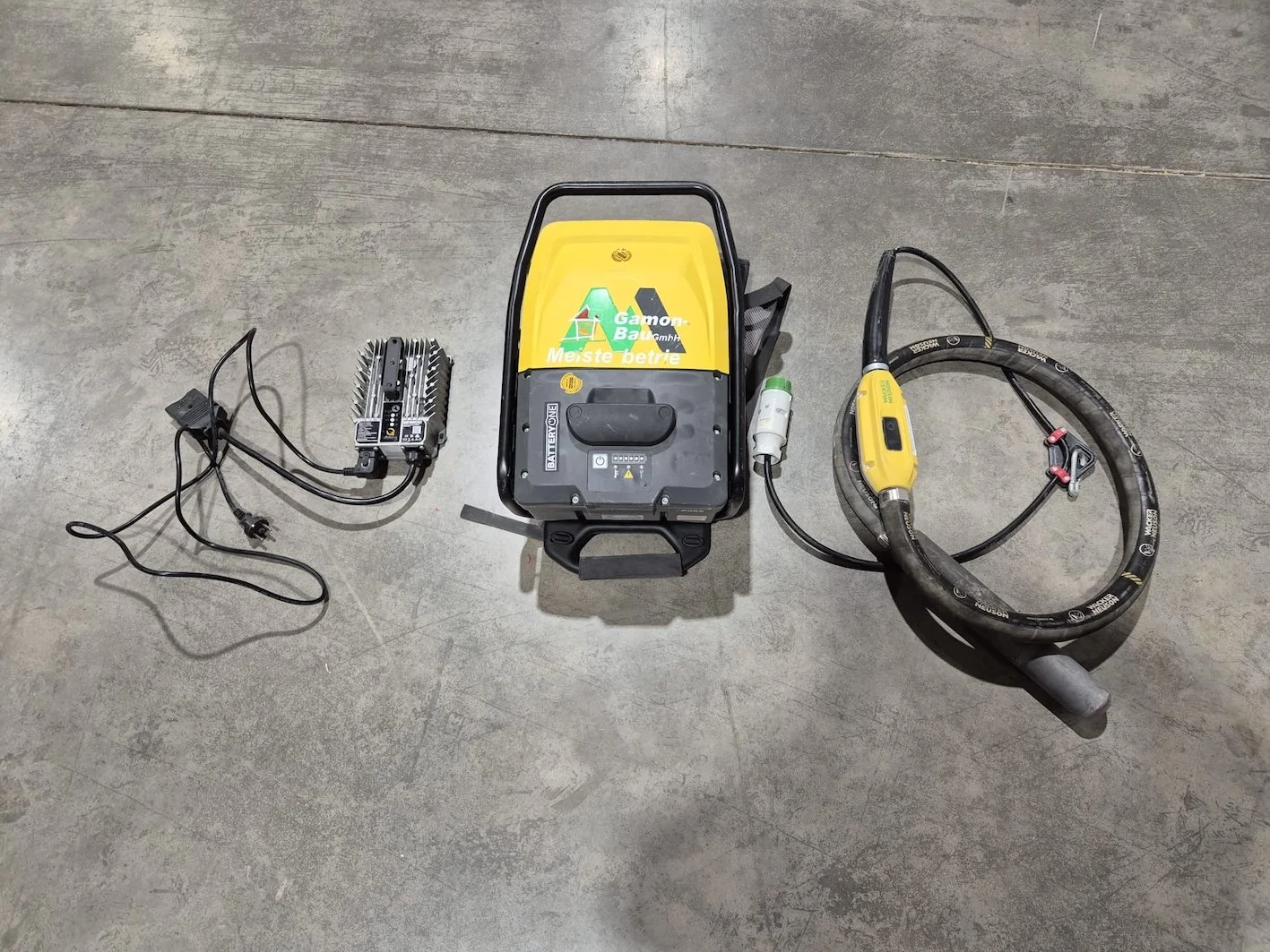 Elektrogerät für das automatische Schleifen oder Schneiden von Beton oder Stein, mit Netzteil, Operationseinheit, und Kabel, auf einer Betonbodenfläche.