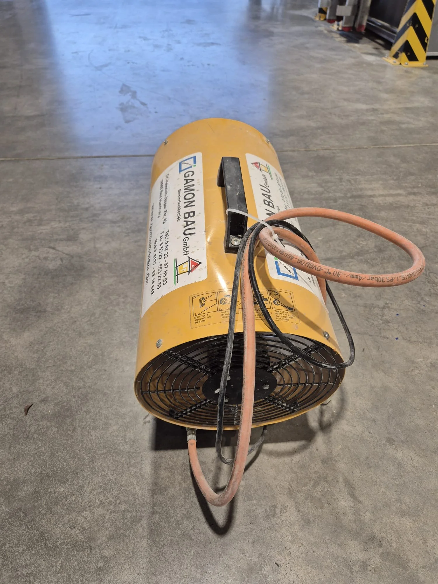 Ein gelber Heizlüfter mit Kabel auf einem Betonboden in einer Garage oder Werkstatt.