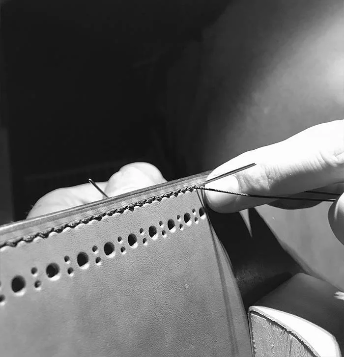 Nahaufnahme einer Person beim Nähen eines Lederartikels.