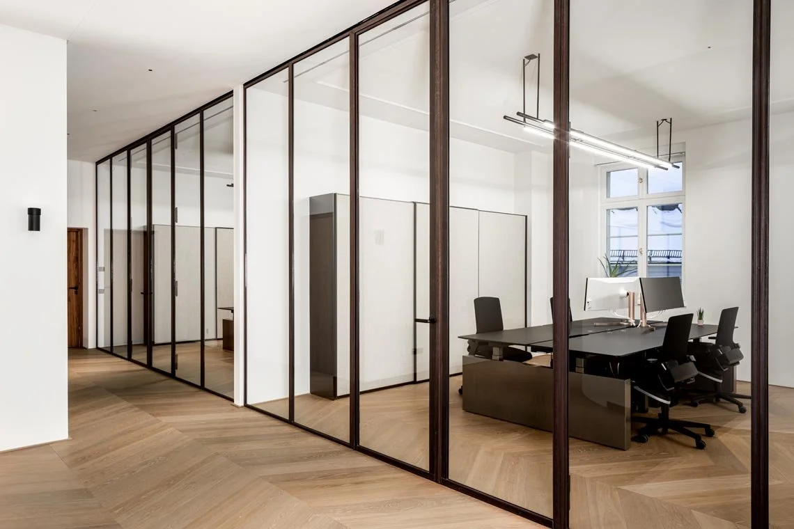 Moderner Büroraum mit Glaswänden, Arbeitsplätzen, Computern und Stühlen.