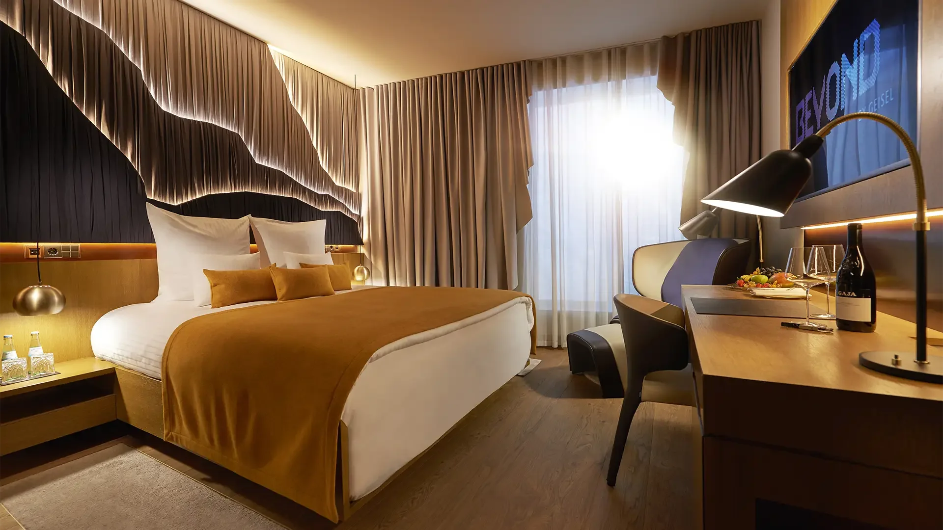 Ein modernes Hotelzimmer mit einem großen Bett, einem Schreibtisch, Stühlen, Vorhängen, Beleuchtung und einem Fernseher.