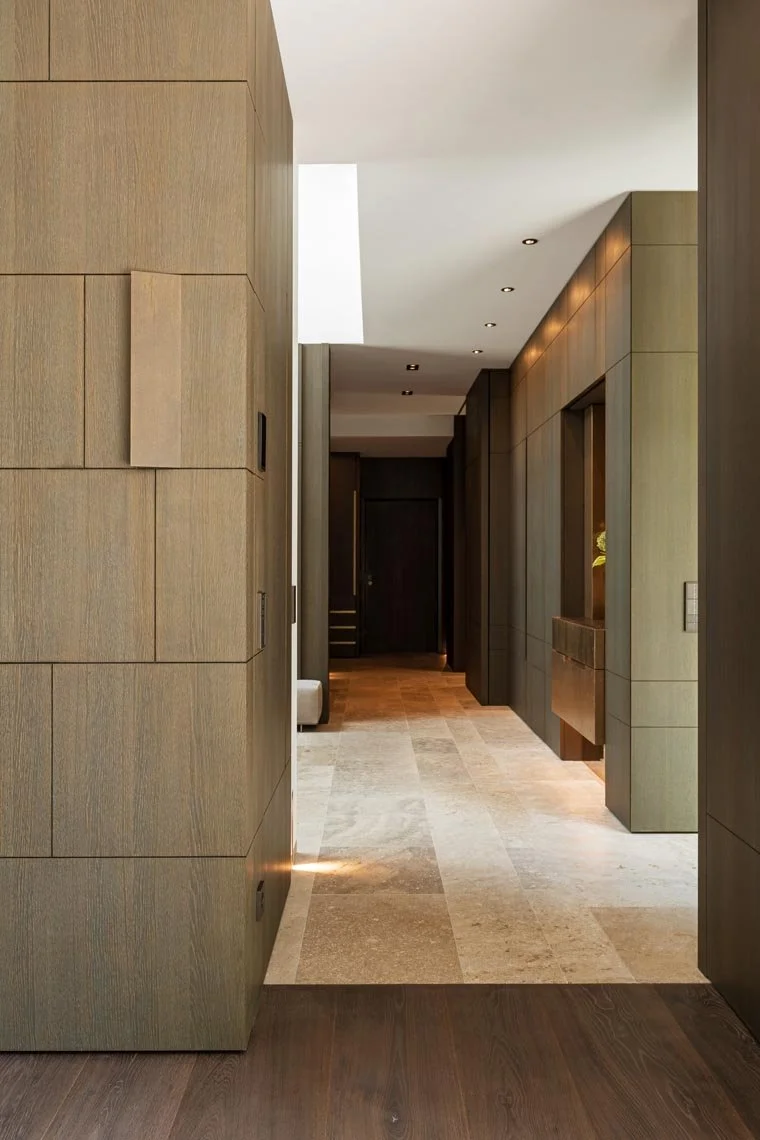 Innenansicht eines modernen Flurs mit Holzverkleidung, dunklen Türen und einem hellen Deckenlicht.