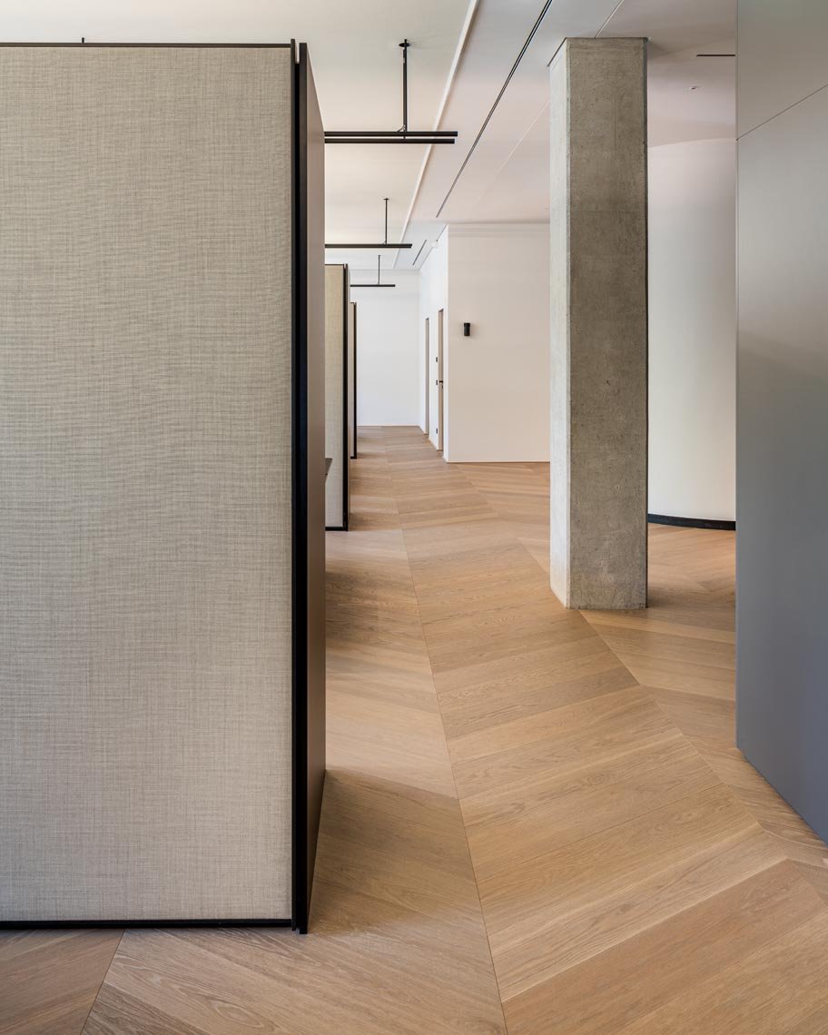 Innenaufnahme eines modernen, minimalistischen Flures mit Holzfußboden, mehreren weißen Türen, einer Betonstütze und Deckenleuchten.