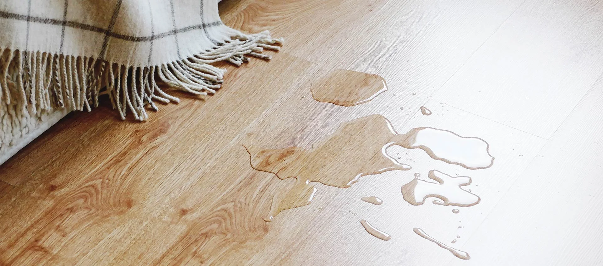 Wasserpfütze auf einem hölzernen Boden, neben einem Teppich.