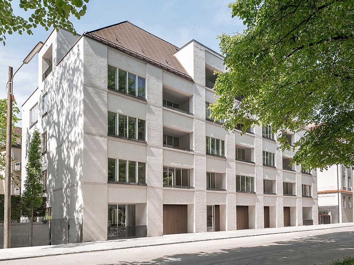 Mehrstöckiges modernes Wohngebäude mit weißen Wänden und mehreren Balkonen, Bäumen und Straßenlaterne in der Nähe.