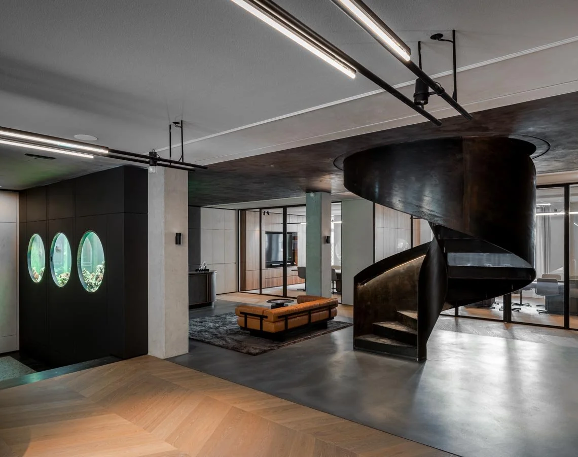 Innenansicht mit spiralförmiger dunkler Treppe, modernen Sitzmöbeln und Aquariumfenstern im Wohnzimmer.