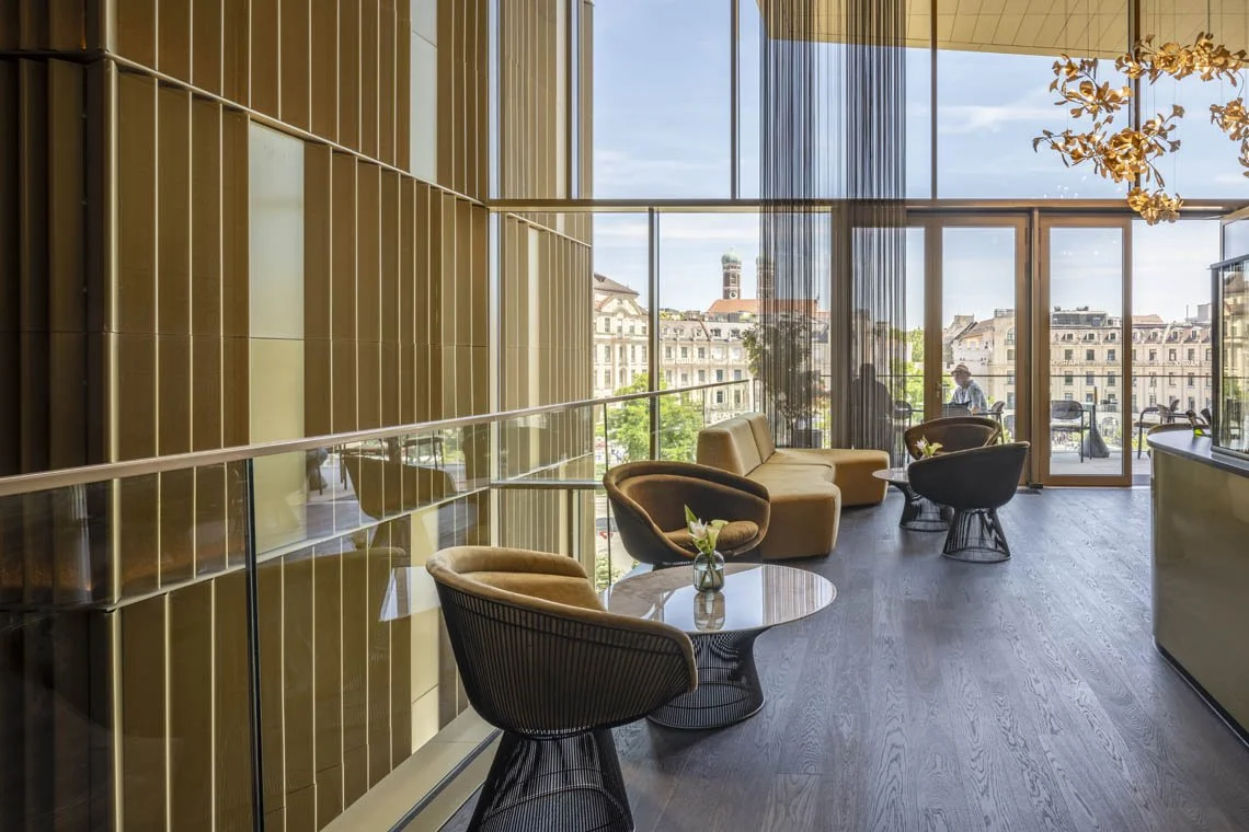 Ein stilvoll eingerichteter Innenraum mit großen Fenstern, Sitzgelegenheiten und Blick auf eine Stadt.