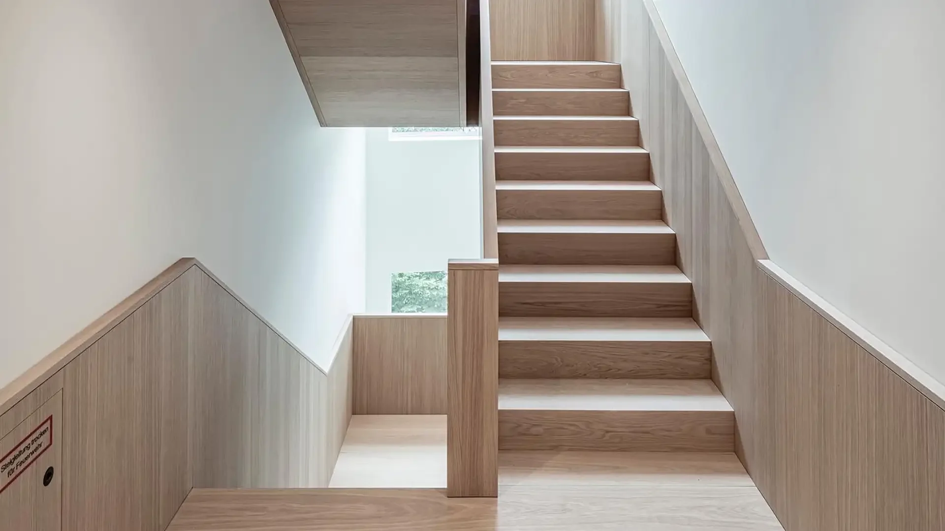 Holztreppe mit weißen Hölzern und einem Fenster im Hintergrund, Blick nach oben