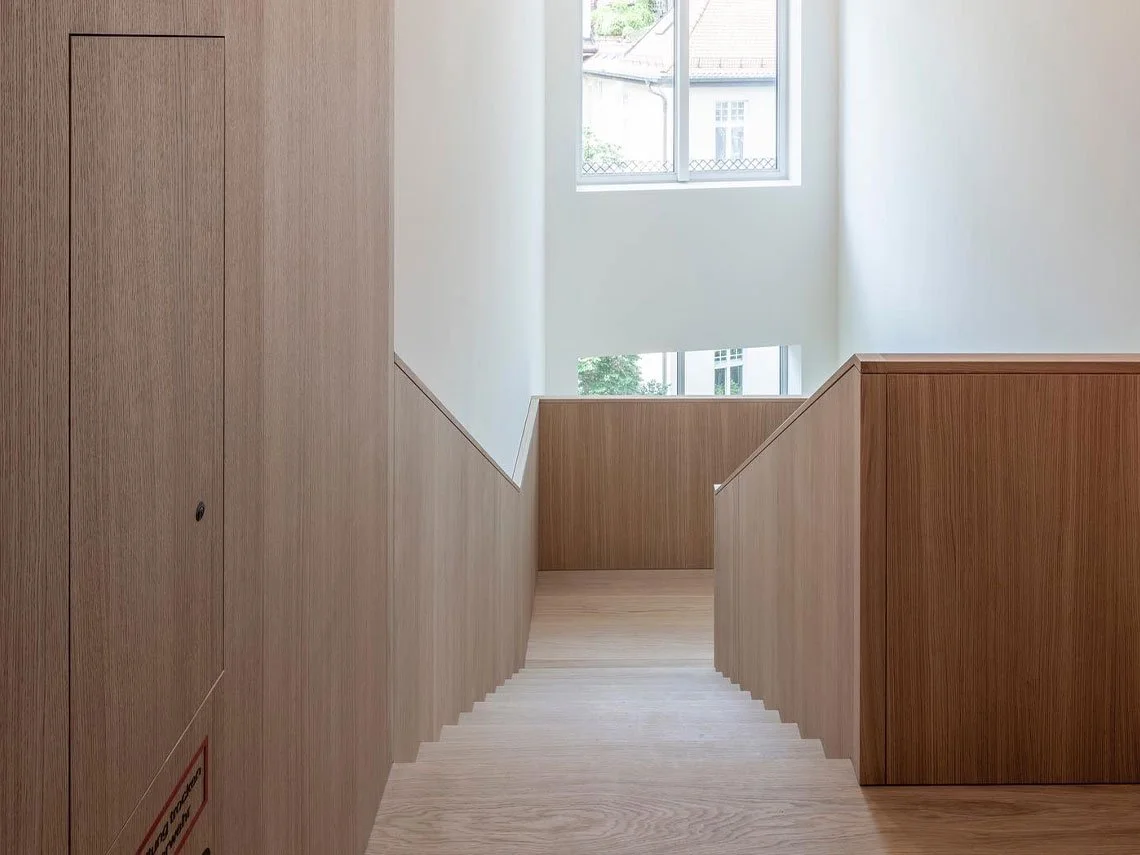 Innenansicht mit Holzwandertreppe, Fenster und natürlichem Licht in einem modernen Gebäude.