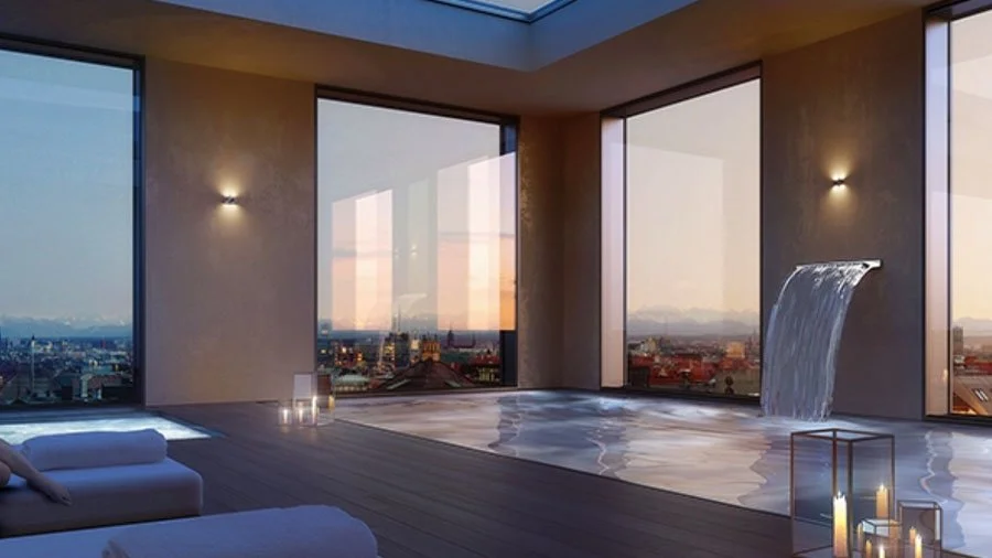 Moderner, eleganter Raum mit großen Fenstern, Wasserfall und Blick auf die Stadt bei Sonnenuntergang, inklusive Kerzen und Sonnenliegen.