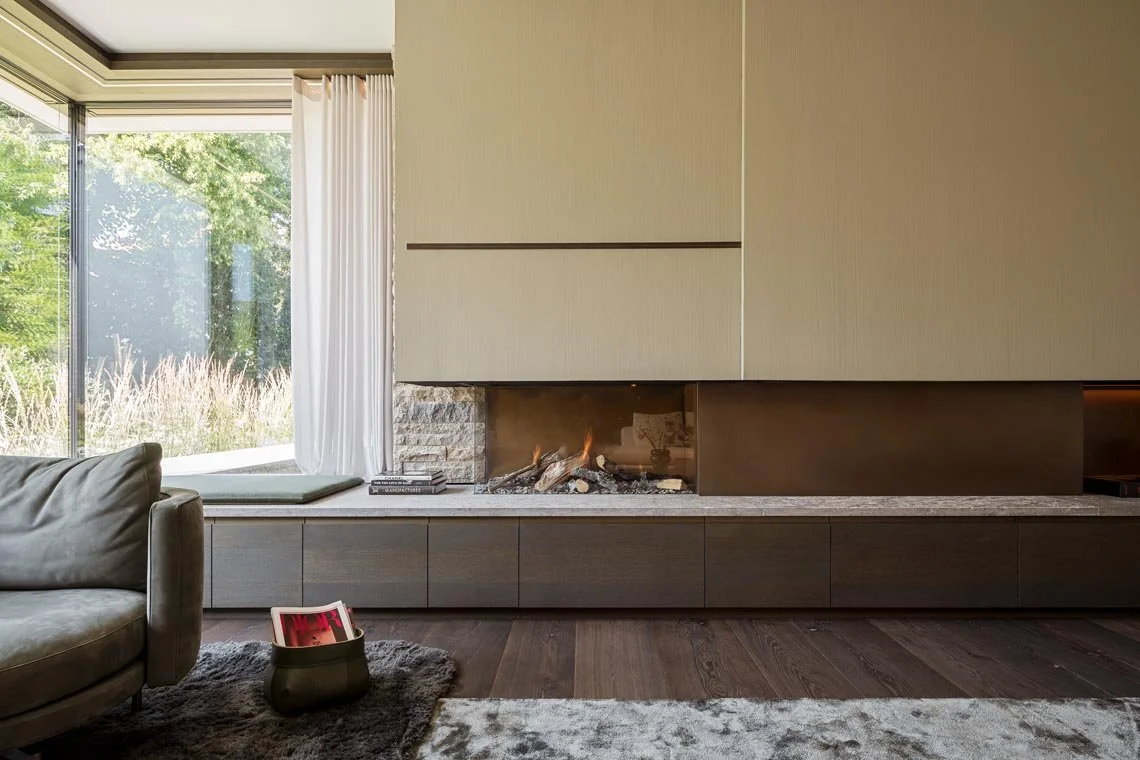 Moderner Wohnzimmerbereich mit Kamin, großen Fenstern, Sofa und dekorativen Elementen.