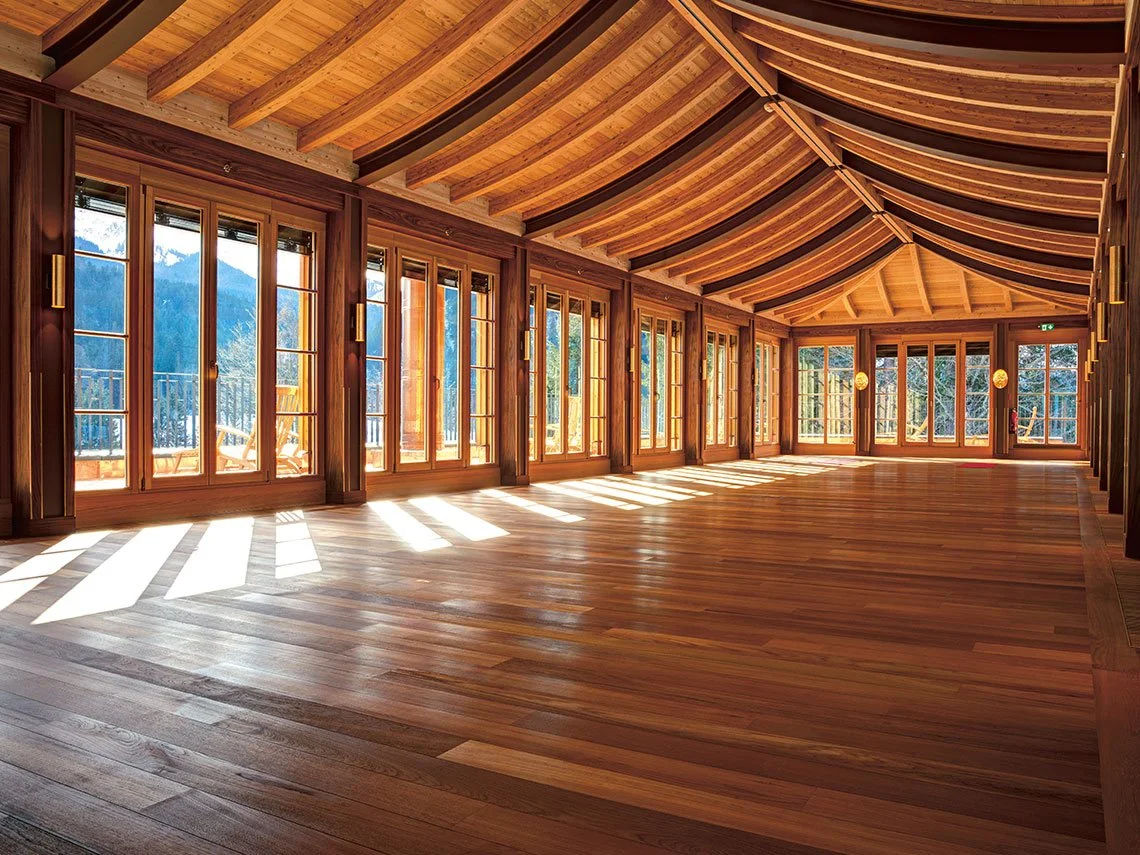 Ein heller, geräumiger Raum mit großen Fenstern und einer Holzbalkendecke, der viel Sonnenlicht durchlässt.