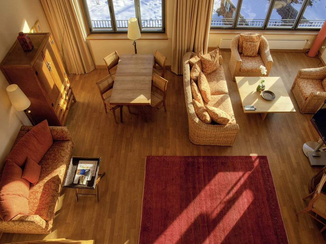 Heller Wohnraum mit Holzboden, Sofa, Sesseln, Couchtisch, Essbereich, großen Fenstern mit Blick auf das Wasser, und Teppich.